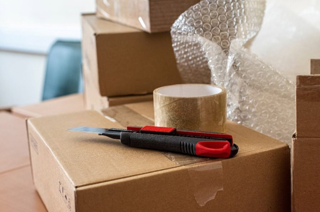 Bastelmesser und durchsichtiges Klebeband auf dem Verpackungskarton